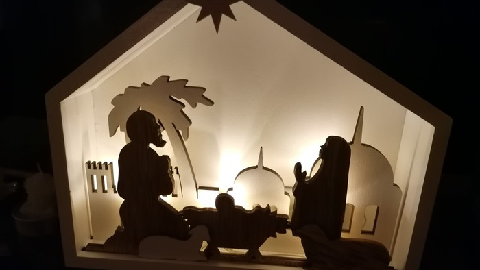 Ein beleuchtetes Scherenschnitt-Nativity-Szene mit Maria, Josef und Baby Jesus in einer Krippe.