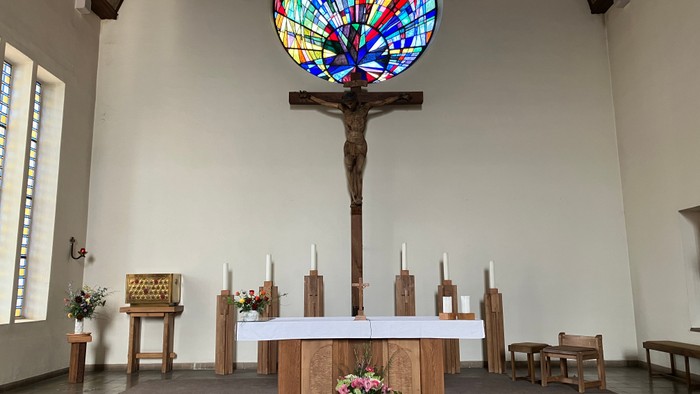 Die Kirche mit einem großen buntem Rundfenster und einem Kruzifix davor
