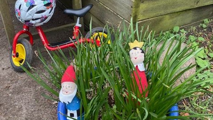 Im Garten stehen zwei Gartenzwerge in einem blauen Reifen, daneben ein Kinderfahrrad und eine Holzkiste.