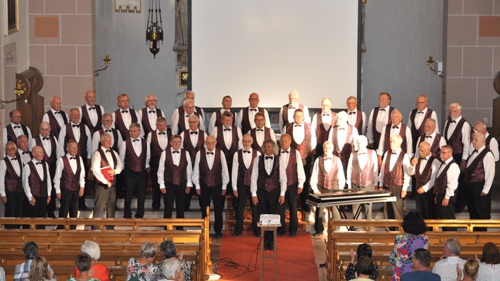 Ein formeller Chorauftritt in einer Kirche mit Publikum, das in Bänken sitzt und aufeinander abgestimmte Kleidung trägt.