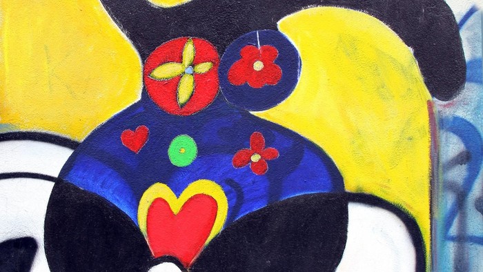 Lebendiges Wandgemälde einer stilisierten Figur mit farbenfrohen geometrischen Mustern und abstrakten Designelementen.