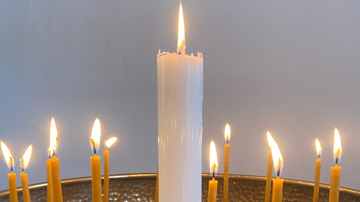 Elegant lysestage med et centralt hvidt lys omgivet af mindre gule lys i en tekstureret skål.