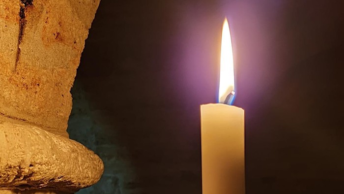 Eine Kerze brennt in einem schwarzen Halter an einer Steinwand.