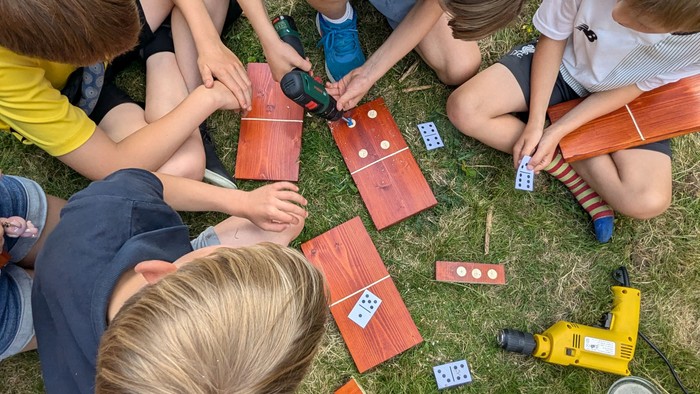 Kinder spielen im Gras mit Dominosteinen und Werkzeug.