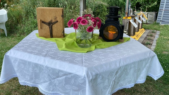Ein Tisch im Freien mit Tischdecke, Blumen, Kerze und Holzkreuz