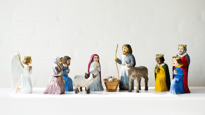 En rekke julefigurer, inklusiv engle, kvinder og dyr, stillet op på en hvid underlag