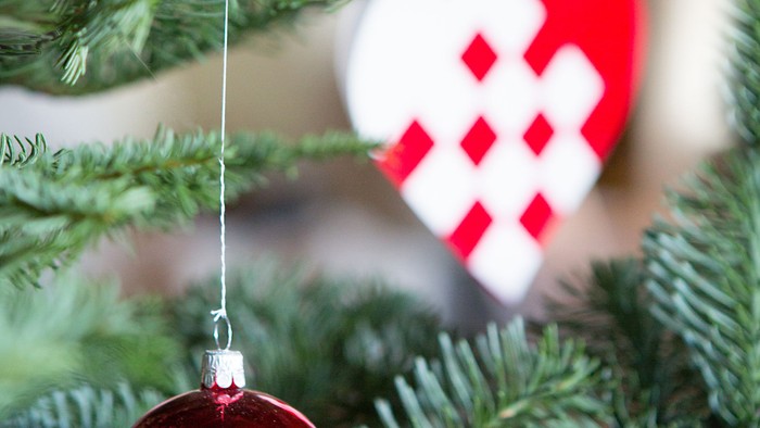 En rød glaskugle hænger på en julgran sammen med et hjerteformet pynt.