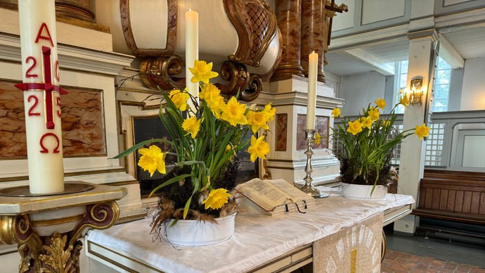 Eleganter Altar, geschmückt mit gelben Blumen, Kerzen und religiösen Symbolen in einer ruhigen Kirchenatmosphäre.