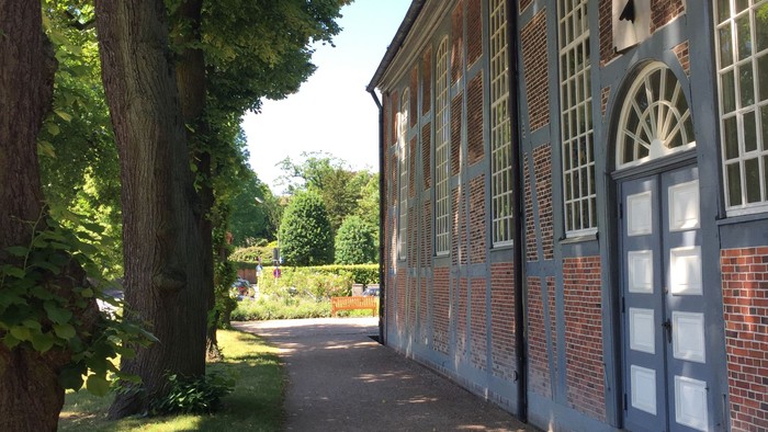 Ein malerischer Pfad führt an einem historischen Backsteingebäude mit dekorativen weißen Fensterrahmen und üppigem Grün vorbei.