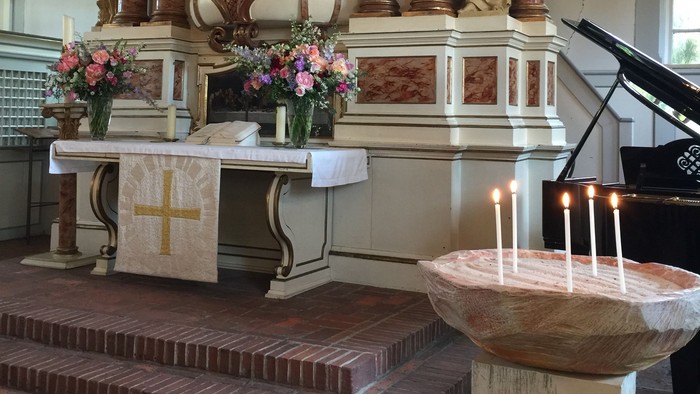 Altar in Kirche mit Kerzen und Blumen, Taufbecken und Orgel