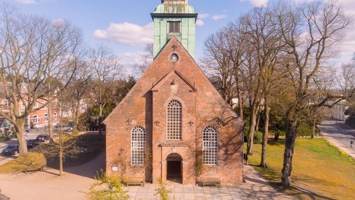 Luftaufnahme einer charmanten Backsteinkirche, umgeben von kahlen Bäumen und einer ruhigen Parkanlage.