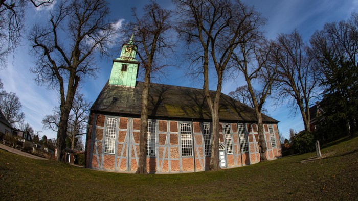 Ein Kirchengebäude mit grünem Turm und bunten Glasfenstern, umgeben von kahlen Bäumen