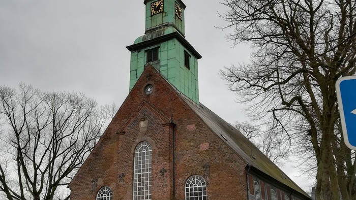 Kirchengebäude aus Ziegeln mit grünem Turm und Uhr.