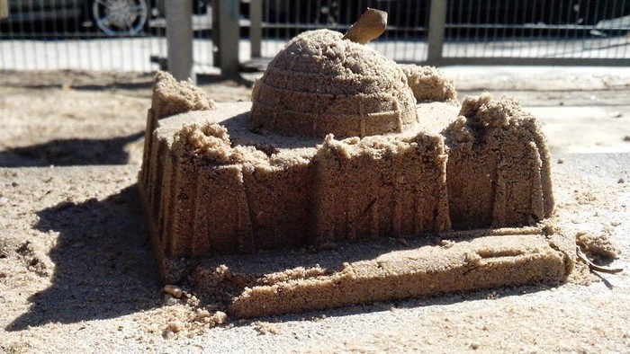 Ein Sandkuchen in Form einer Burg auf einem Sandkasten.