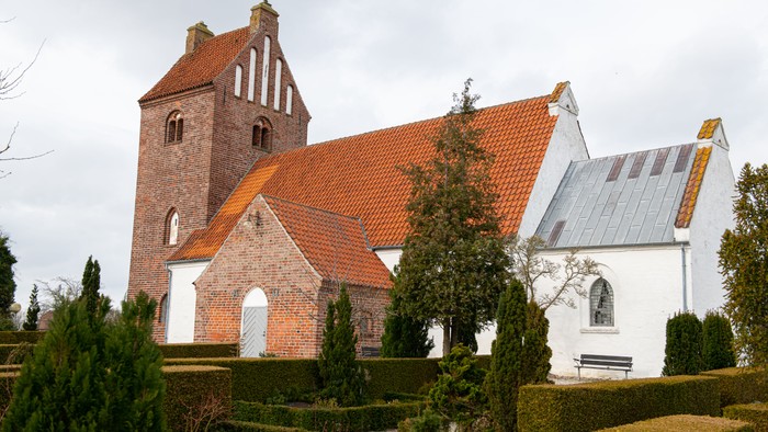 En smuk kirke med røde tag og hvide murværker, omgivet af grønne planter og buske