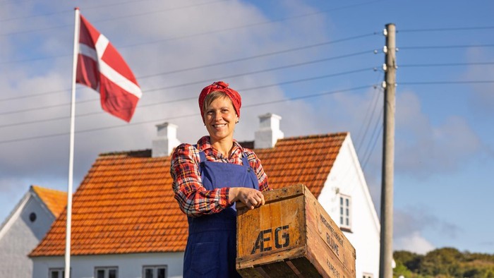 En glad kvinde i overalls bærer en trækasse mærket