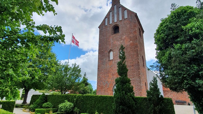En rød murstenstårn med flag i en trædet og grøn have