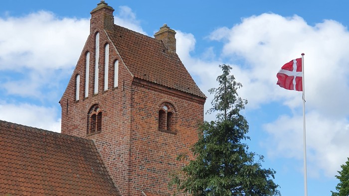 En rød murstenskirke med tårn og en dansk flag på en stang foran
