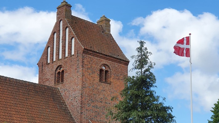 En rød murstenskirke med tårn og en dansk flag på en stang foran