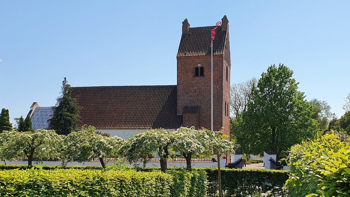 En rød murstenskirke med tårn og en delvis skjult kapel i en grøn og blomstrende have