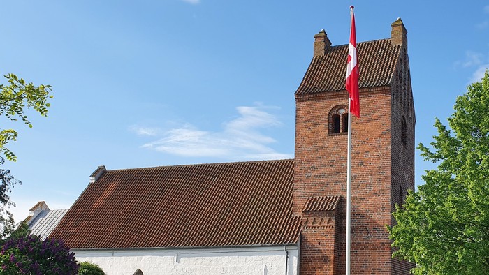 En rød murstenskirke med tårn og flag.