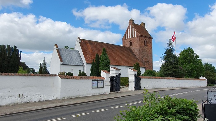 En hvid mur omgiver et rødt teglhus med en canadisk flag på en stang ved siden af en vej