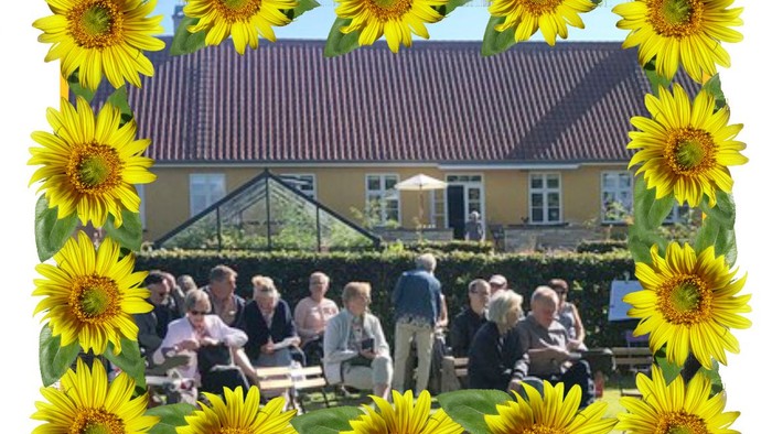 En munter udendørs sammenkomst omgivet af solsikker foran et idyllisk gult hus.