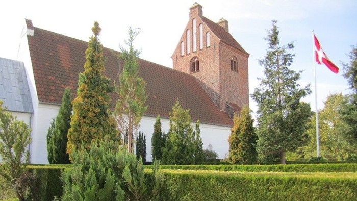 En rødtaget kirke med tårn og en dansk flagvåben på en klar dag