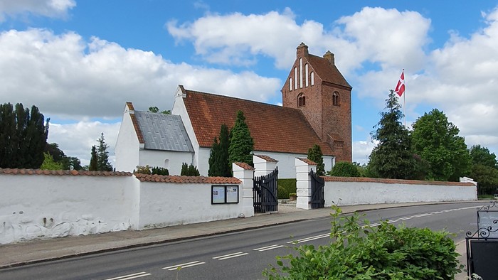 En hvid mur omgiver et rødt teglhus med en canadisk flag på en stang ved siden af en vej