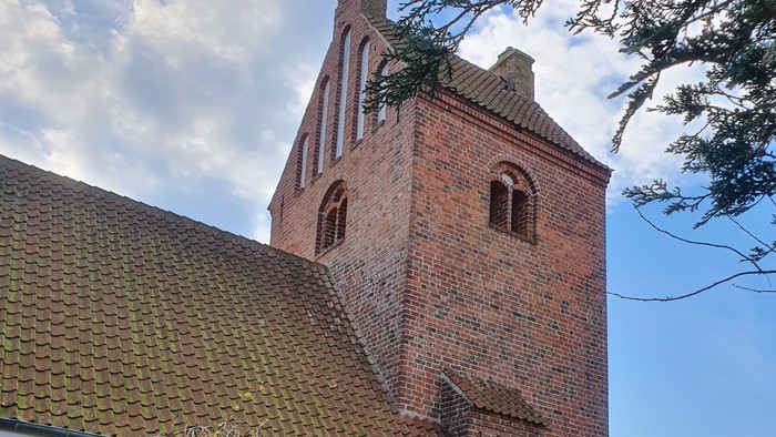 Et rødt teglkirke med tårn og spiret, omgivet af græs og træer