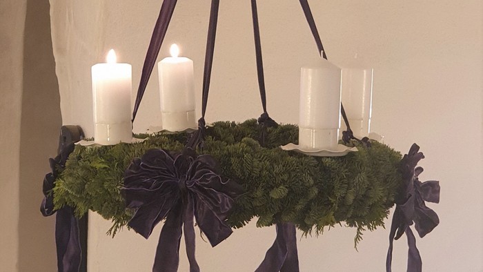 En hængende kranse med grønne blader og fire lyse lygter, smykket med sorte bælter