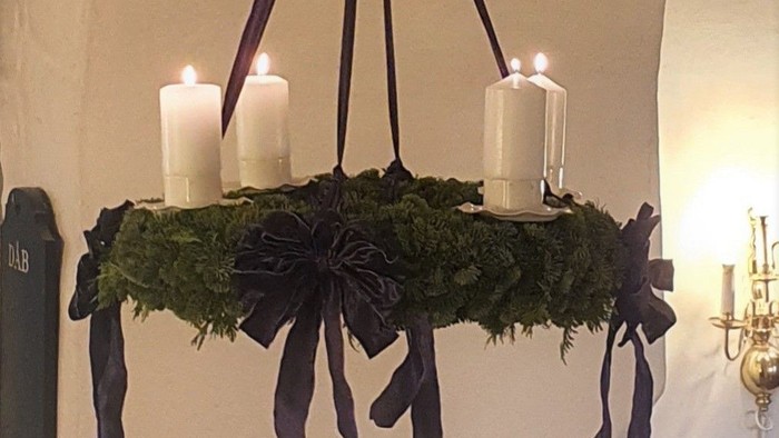 En hængende kranse med grønne blade og sorte bænder med tre lysstaker.