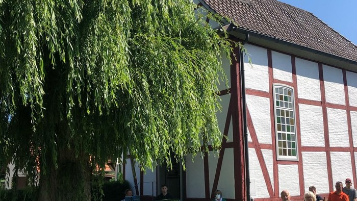 Menschen sitzen draußen vor einer Kirche mit einem Baum.