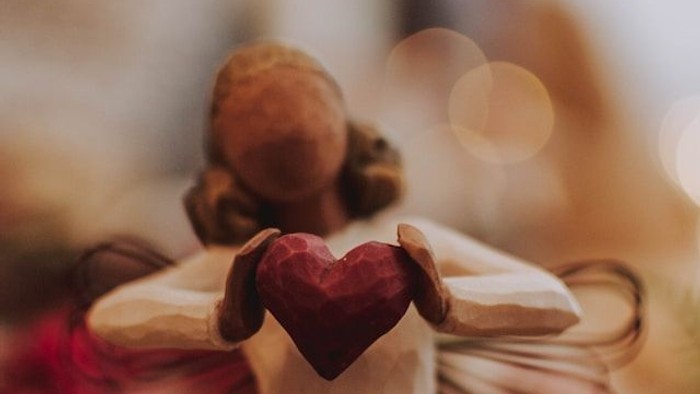 Engelsfigur hält Herz, umgeben von Weihnachtsdekoration