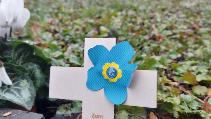 Blauer Blumenaufkleber auf weißem Kreuz im Friedhof