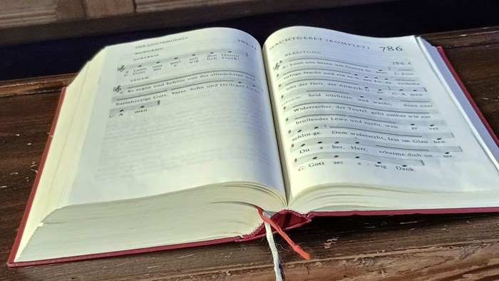 Ein offenes Gesangbuch mit deutschen Liedtexten und Noten auf einer hölzernen Oberfläche.
