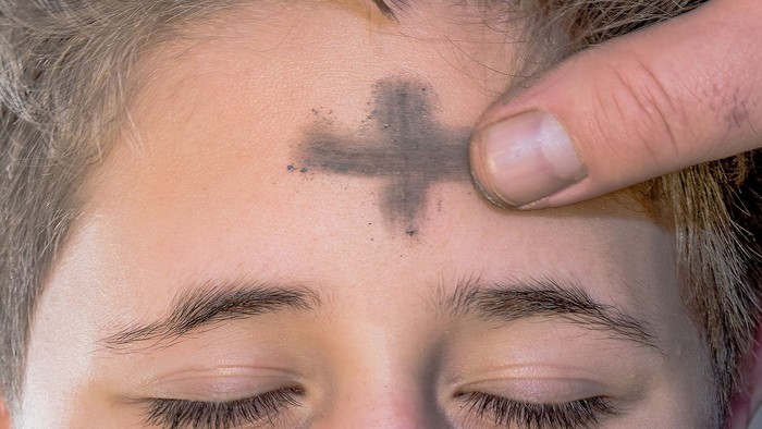 Eine Hand zeichnet ein Kreuz auf die Stirn einer Person.