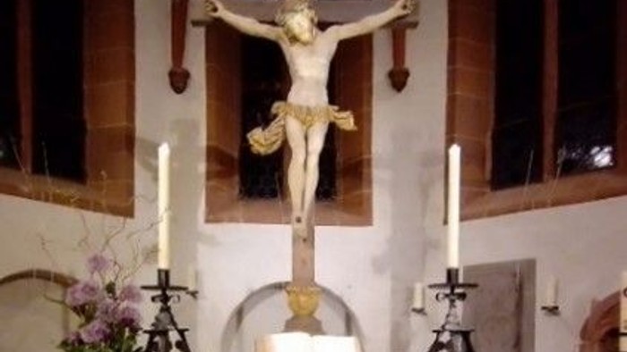 Das Bild zeigt eine Kreuzigungsgruppe in einer Kirche mit Kerzen und Blumen.