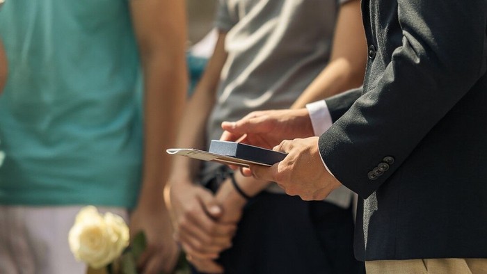 Ein Mann in Anzug hält ein Smartphone und eine Blume.