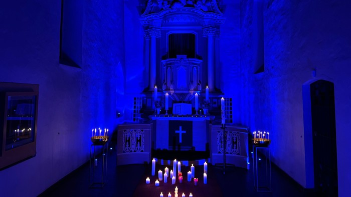 Kirchlicher Raum mit blauer Beleuchtung und zahlreichen Kerzen