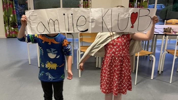 To børn holder et banner med teksten Familieklub op foran deres ansigter.
