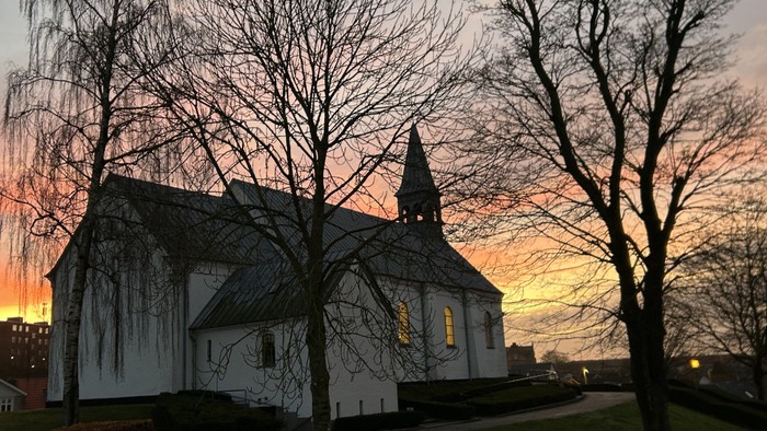 Hvid kirke omgivet af nøgne træer i skumringen