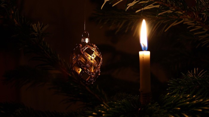Lille tændt juletræslys og kunstig kogle på et juletræ, der står i mørke
