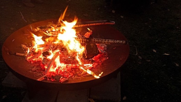 Ein Feuer brennt in einem Metallbecken auf einem Steinboden.