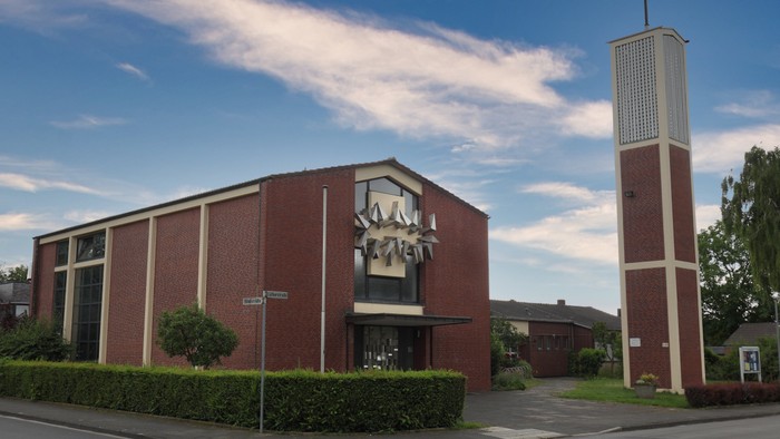 Das Bild zeigt eine Kirche mit hohem Turm und rotem Backsteinbau.