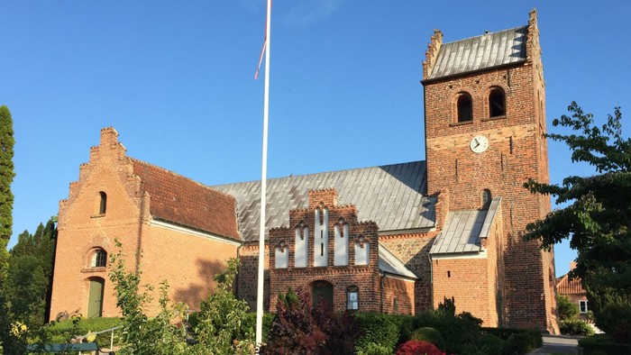 En gammel kirke med klokketårn og en flagstang foran
