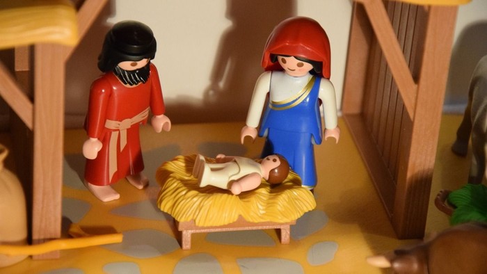 Kleine Figuren in einer Krippe, eine mit rotem Haar, eine mit schwarzem Haar, ein Baby in einer Krippe.