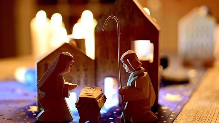Kleine hölzerne Weihnachtskrippe mit Maria, Josef und dem Jesuskind in einem Stall, sanft beleuchtet.