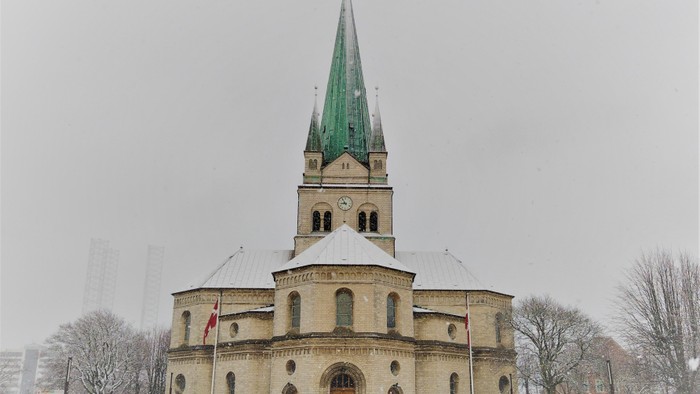 En stor kirke med grøn spire og klokketårn i snefaldt landskab