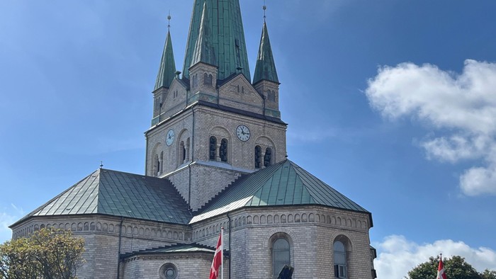 En stor kirke med to spirer og en klokke, med flag i forgrunden